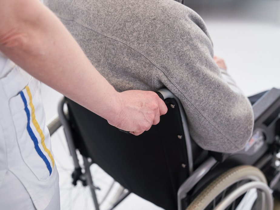 Ein Pflegeassistent schiebt einen Patienten im Rollstuhl.