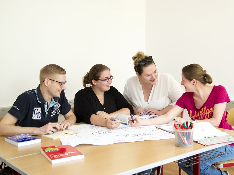 Vier Personen sitzen bei einem Tisch und gestalten ein Plakat.